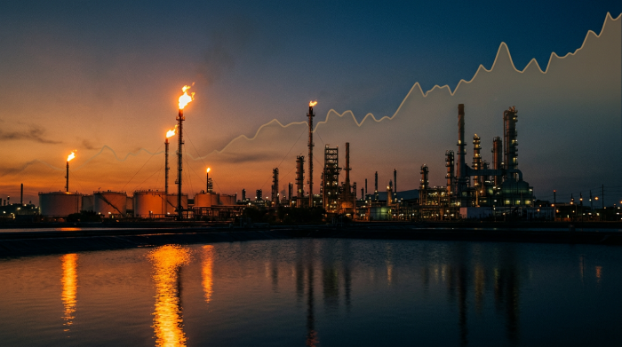 Oil refinery at dusk with flare stacks burning against darkening sky, representing the energy-to-inflation transmission chain